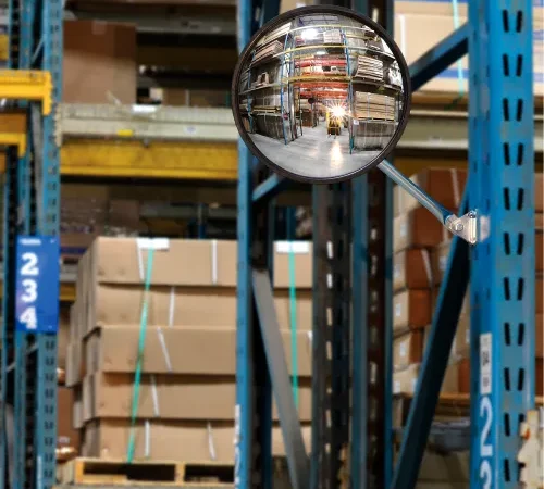 Convex safety mirror reflecting warehouse racks and forklift