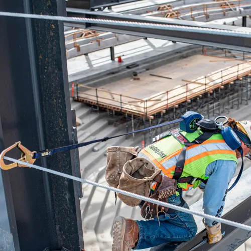 Construction worker wearing safety harness on beam